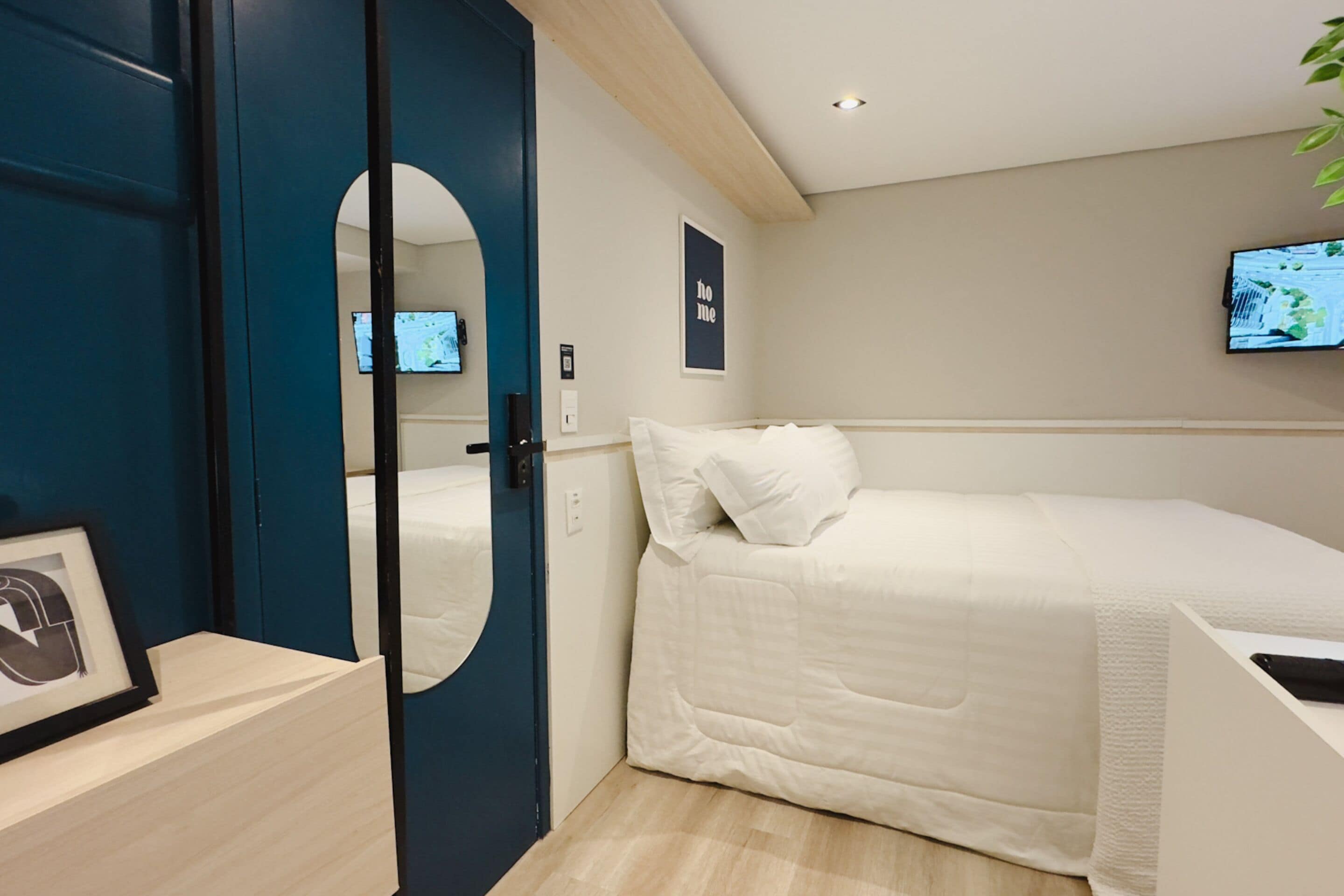 Une chambre d’hôtel moderne équipée d’un lit, d’un téléviseur fixé au mur et d’une porte avec un miroir.