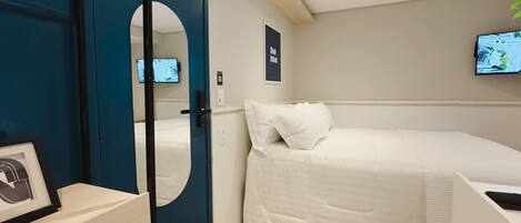 Una habitación de hotel moderna con una cama, un televisor montado en la pared y una puerta con espejo.