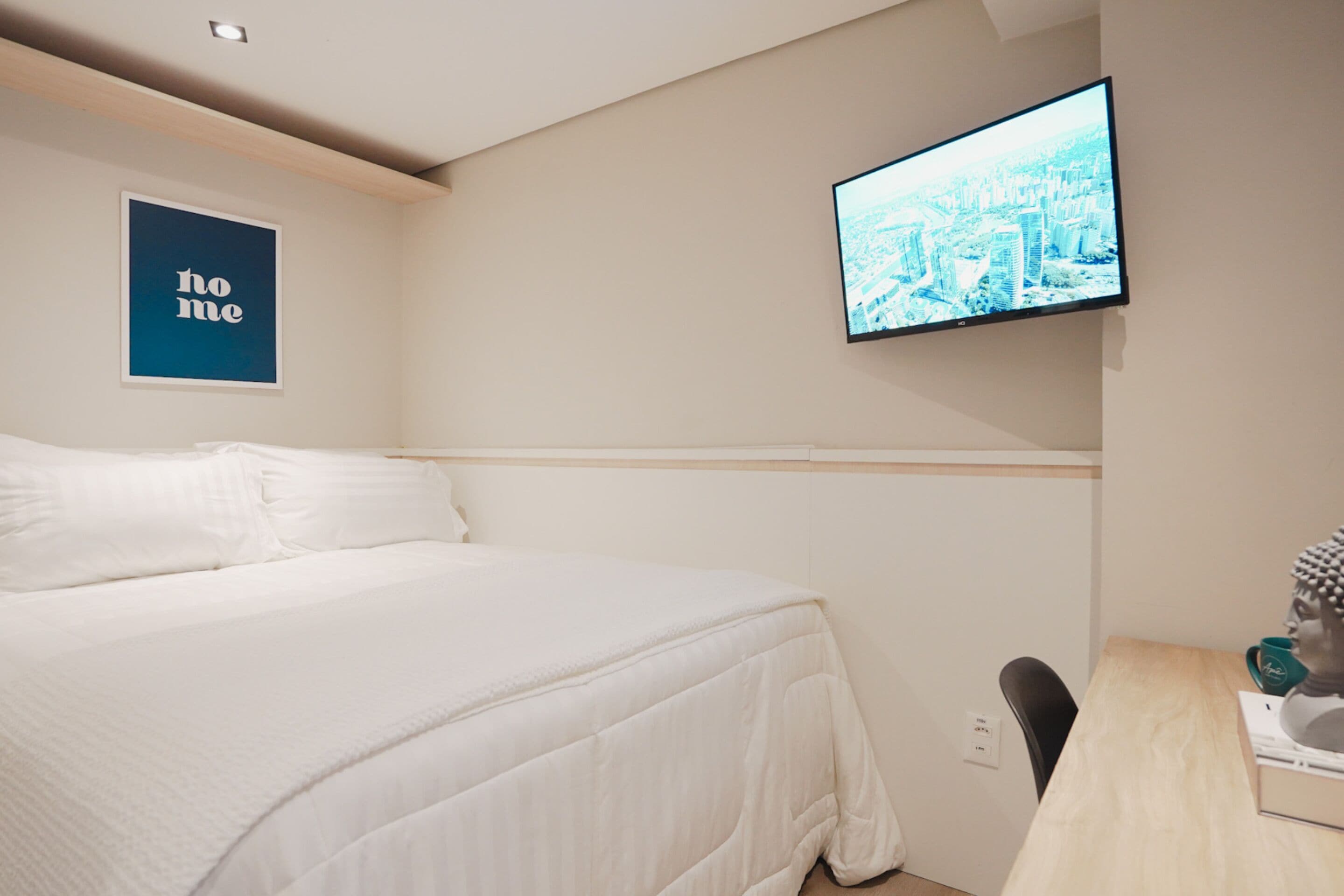 Een slaapkamer met een bed, een bureau, een stoel, een aan de muur bevestigde televisie en een lijst met het woord 'home'.