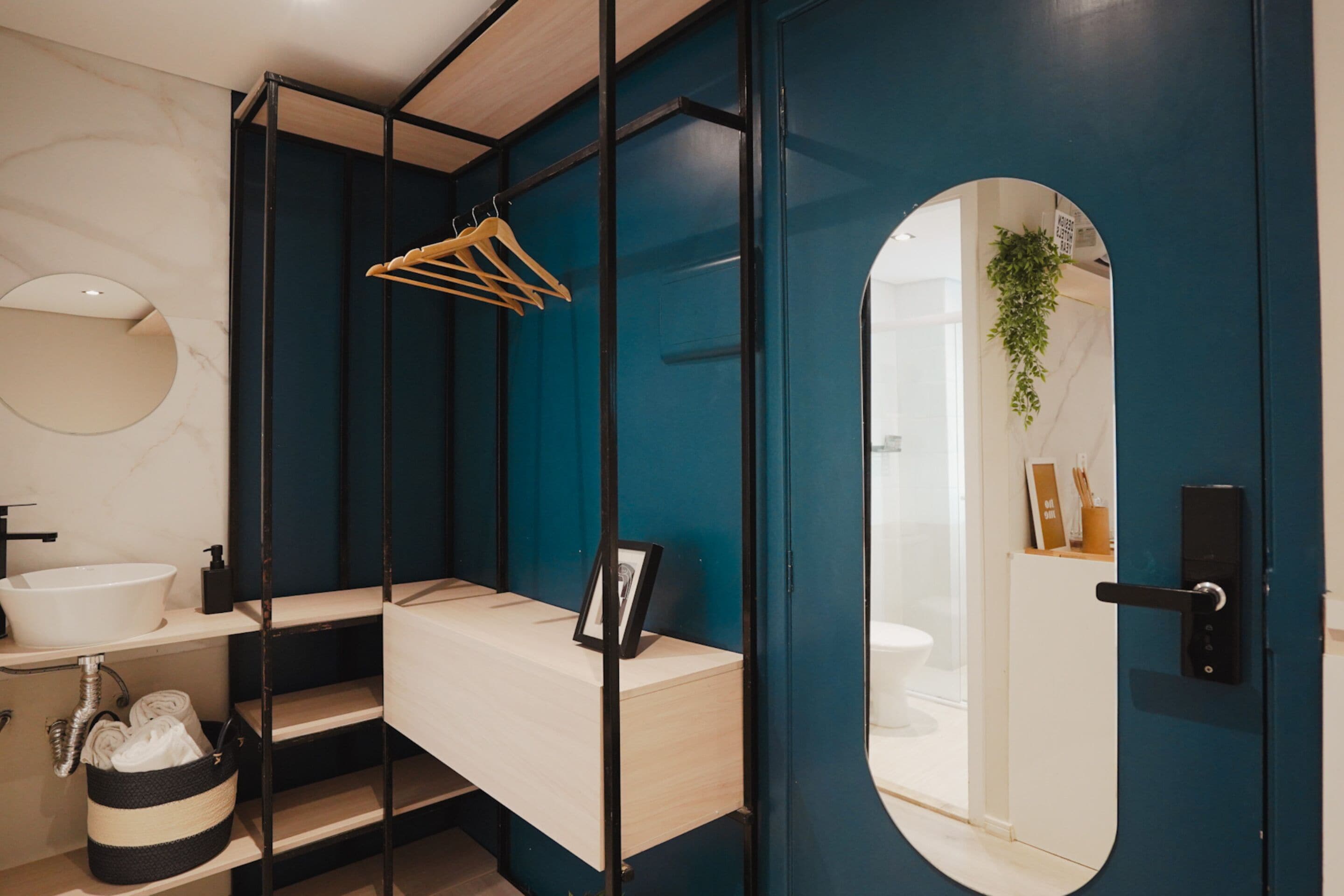 Une salle de bain moderne avec un meuble-lavabo en bois, un miroir rond et une plante suspendue.