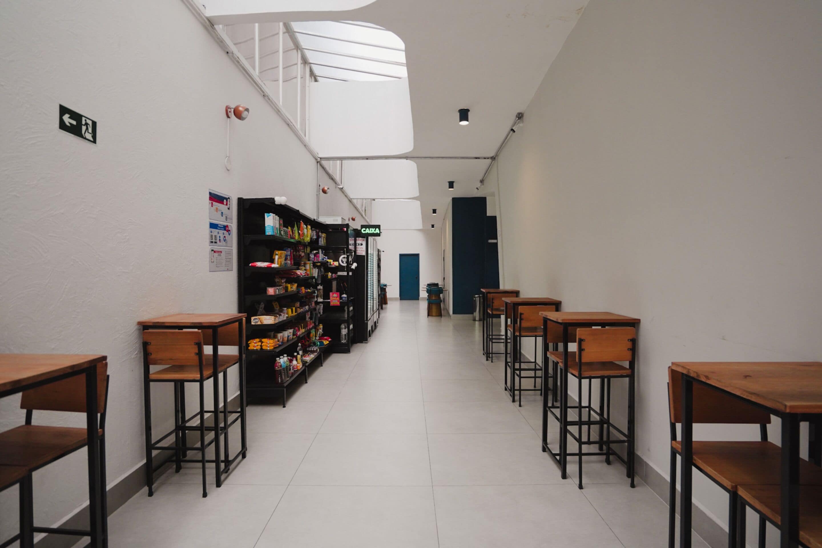 Een gang met houten bureaus en stoelen, een automaat en een trap.