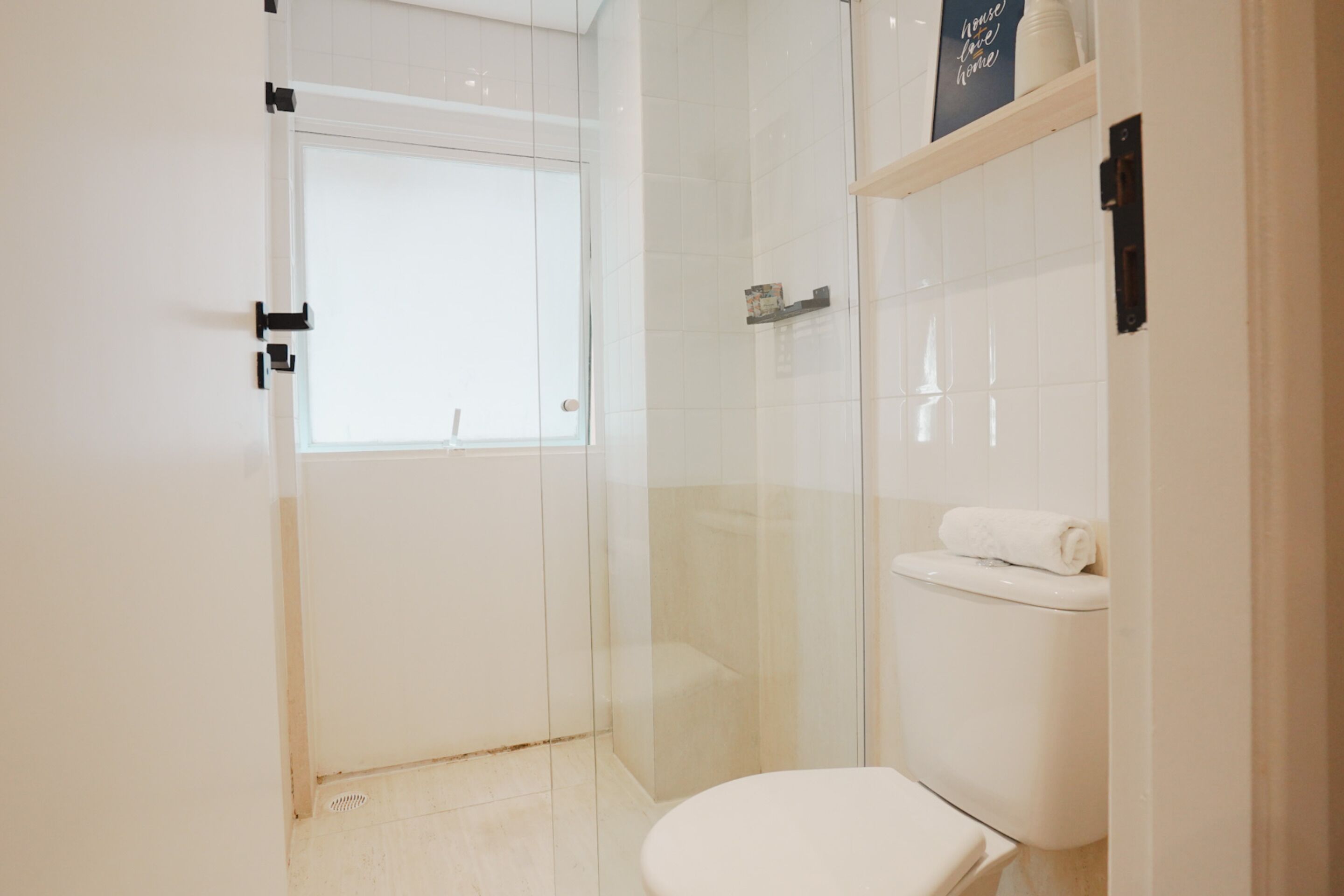 A modern bathroom with a glass shower enclosure, a toilet, and a shelf with toiletries.
