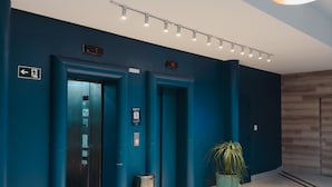 An elevator area with blue walls, a potted plant, and a trash bin. - Apê Bela Cintra (São Paulo)