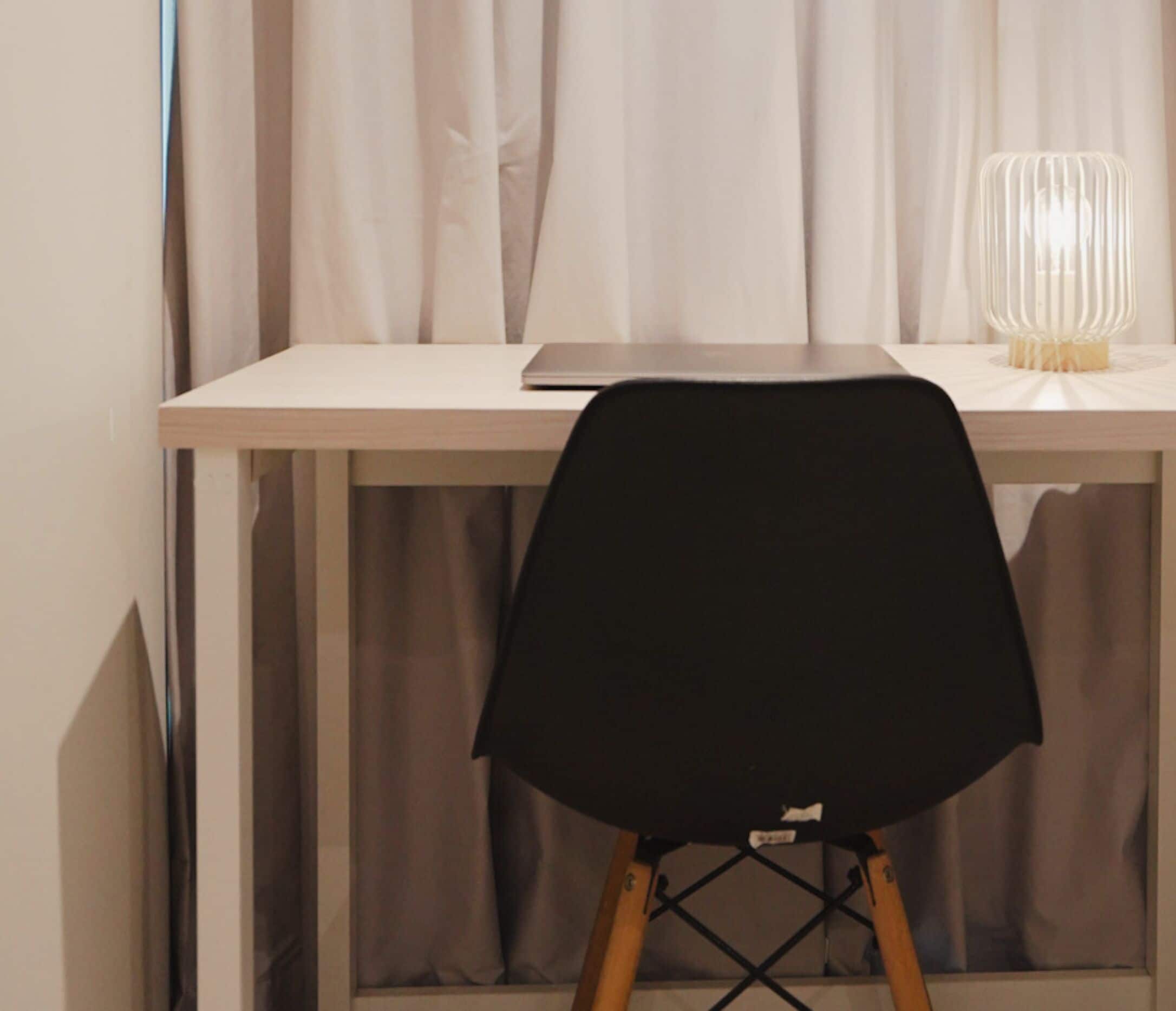 A desk with a laptop, a black chair, and a lamp.