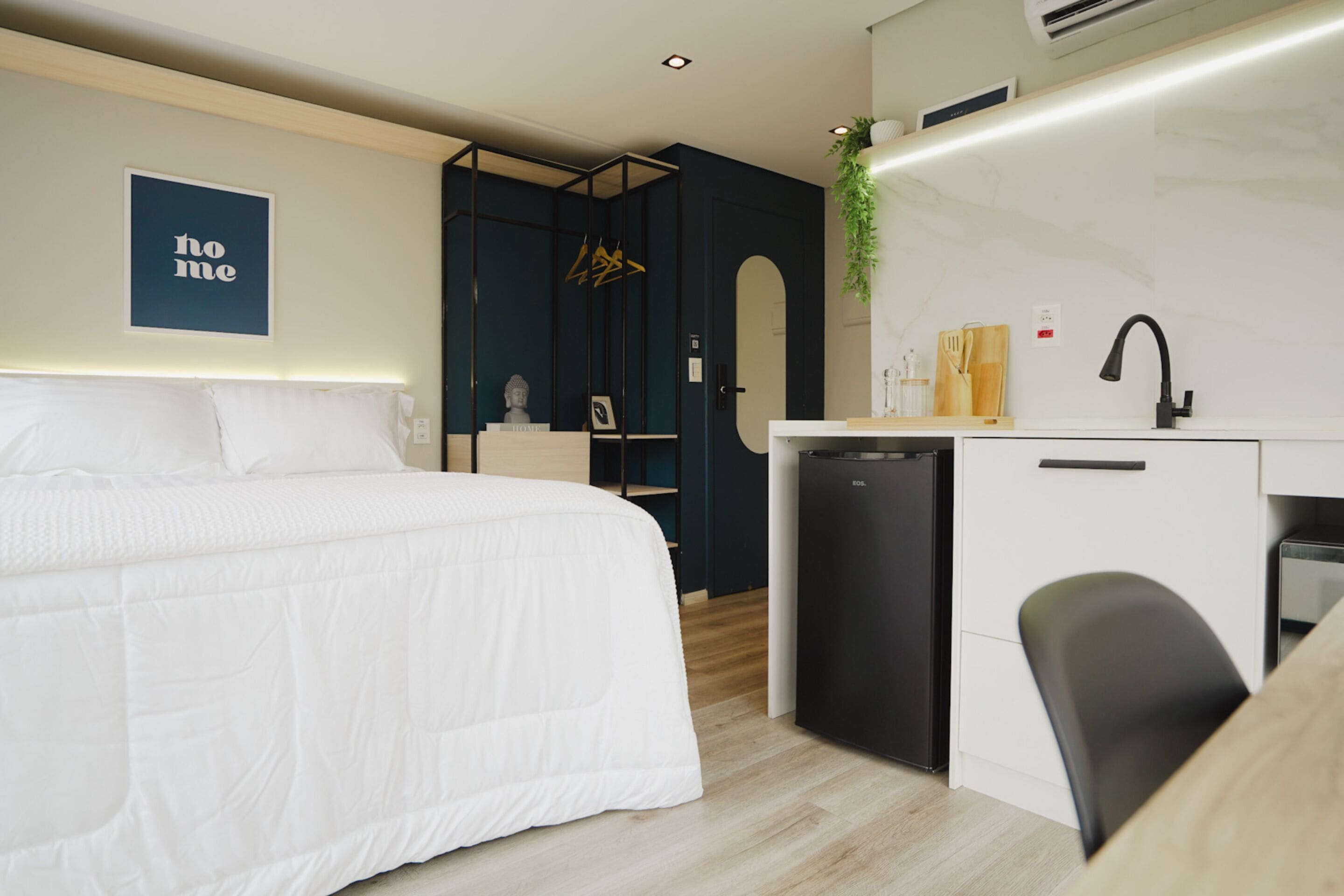 Una habitación de hotel moderna con una cama grande, una kitchenette compacta y un pequeño escritorio.