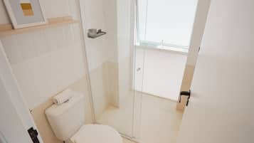 Un bagno con il water, una cabina doccia in vetro e uno scaffale con articoli da toilette.