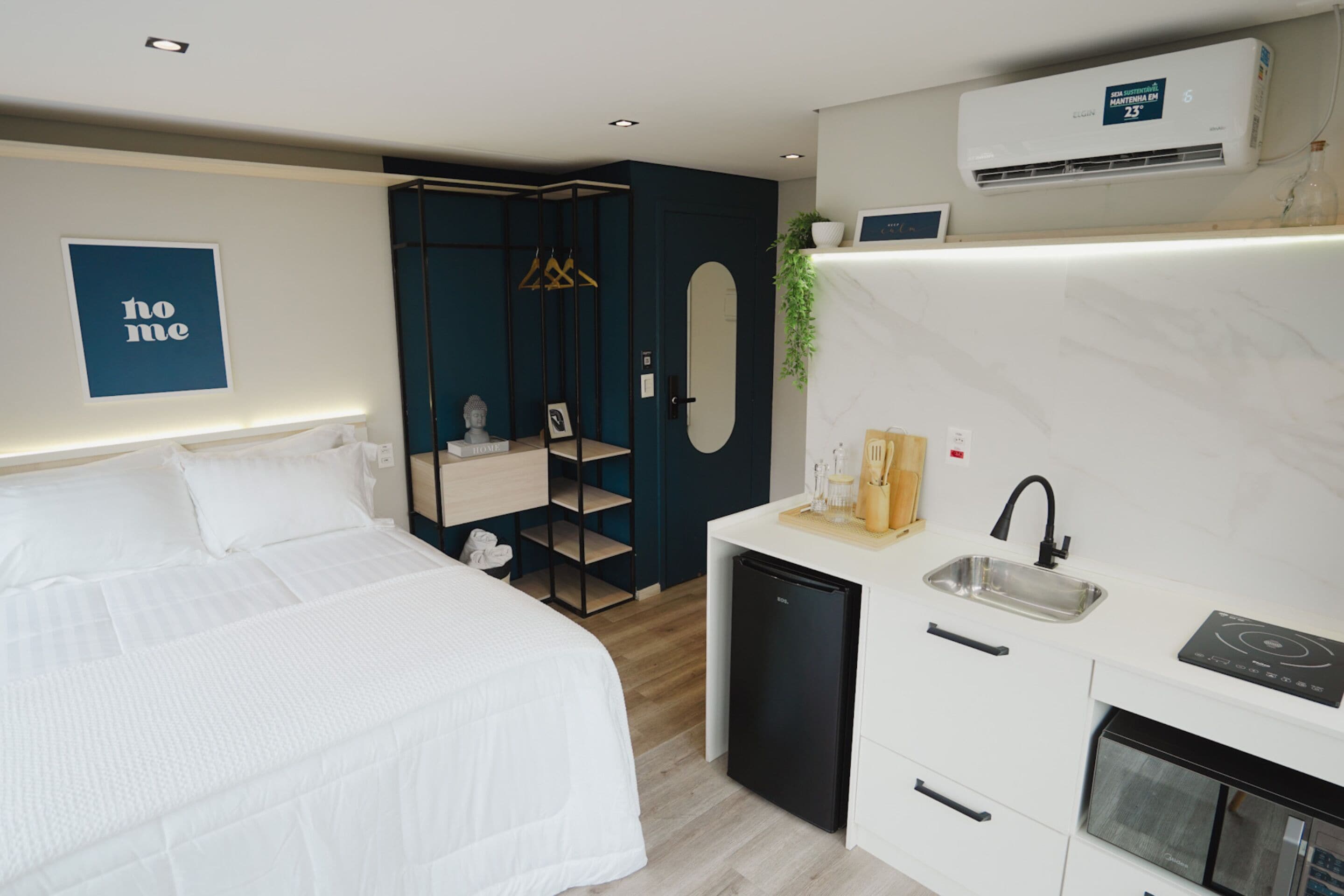 Une chambre d’hôtel compacte comprenant un lit, une petite kitchenette, un miroir et un climatiseur fixé au mur.