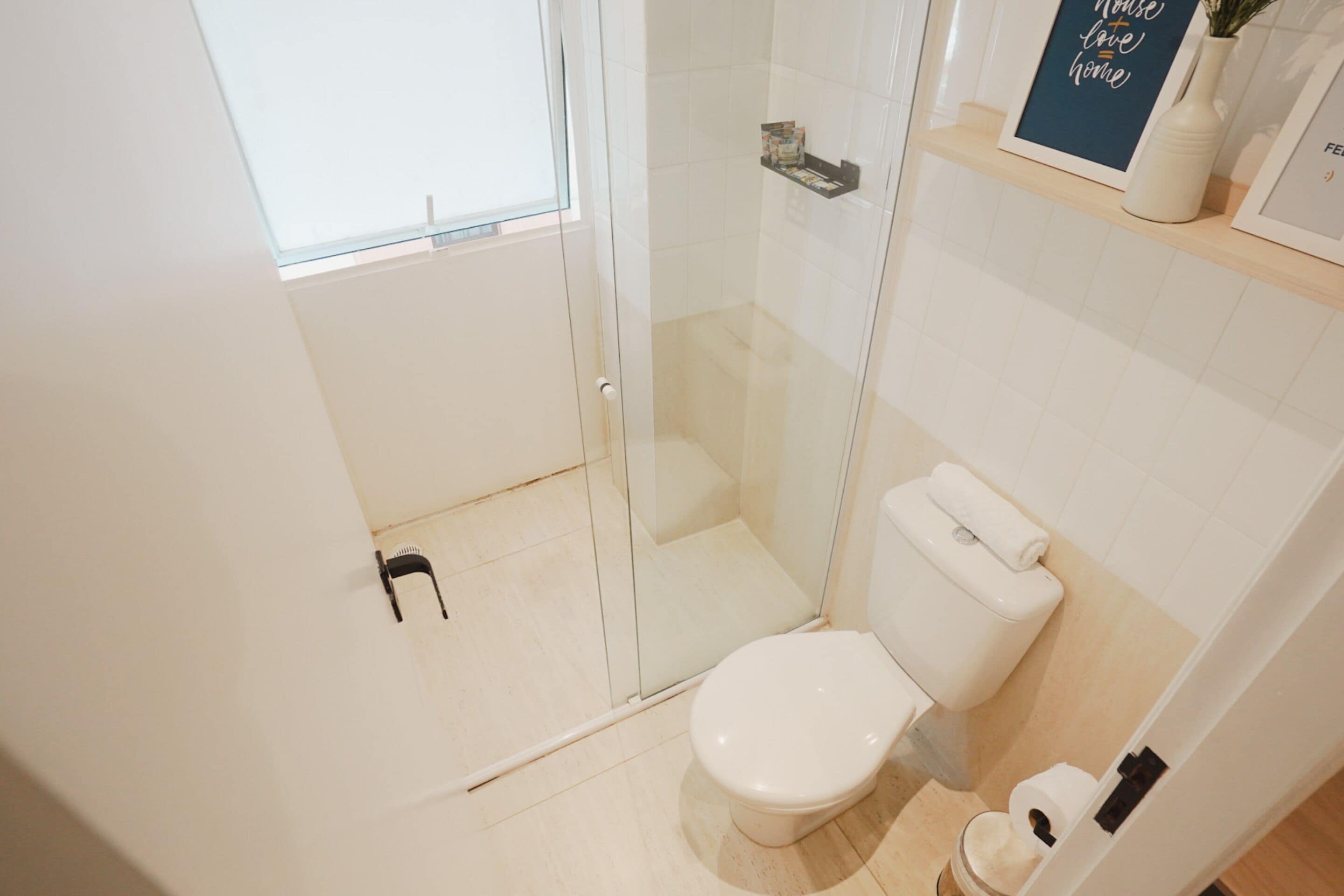 A modern bathroom with a glass shower enclosure, a white toilet, and a shelf with toiletries.