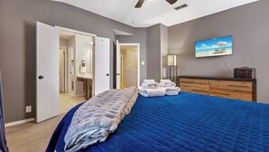 Ein Schlafzimmer mit einem großen Bett, einem Schminktisch, einem Fernseher und einem durch eine offene Tür einsehbaren Badezimmer.