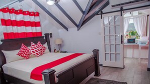 Ein Schlafzimmer mit Bett, Kissen, einem Nachttisch, einer Lampe und Blick ins Freie durch eine Tür.