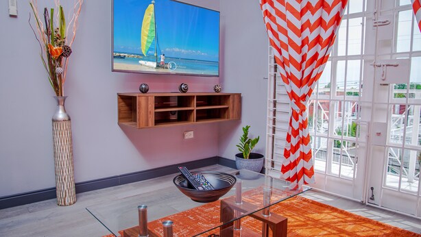 Ein Wohnzimmer mit Fernseher, einer Schale mit Fernbedienung, einer Vase mit Blumen und Blick ins Freie.