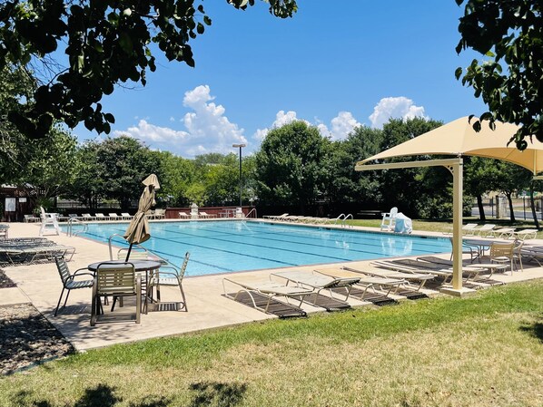 Piscina com espreguiçadeiras e guarda-sóis, cercada por árvores e um céu claro.