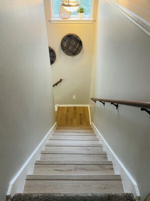 Un escalier en bois avec une rampe, une fenêtre agrémentée d’une plante et des œuvres d’art décoratives murales.