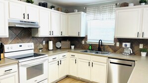Una cocina moderna con armarios blancos, horno empotrado, pileta y cafetera.
