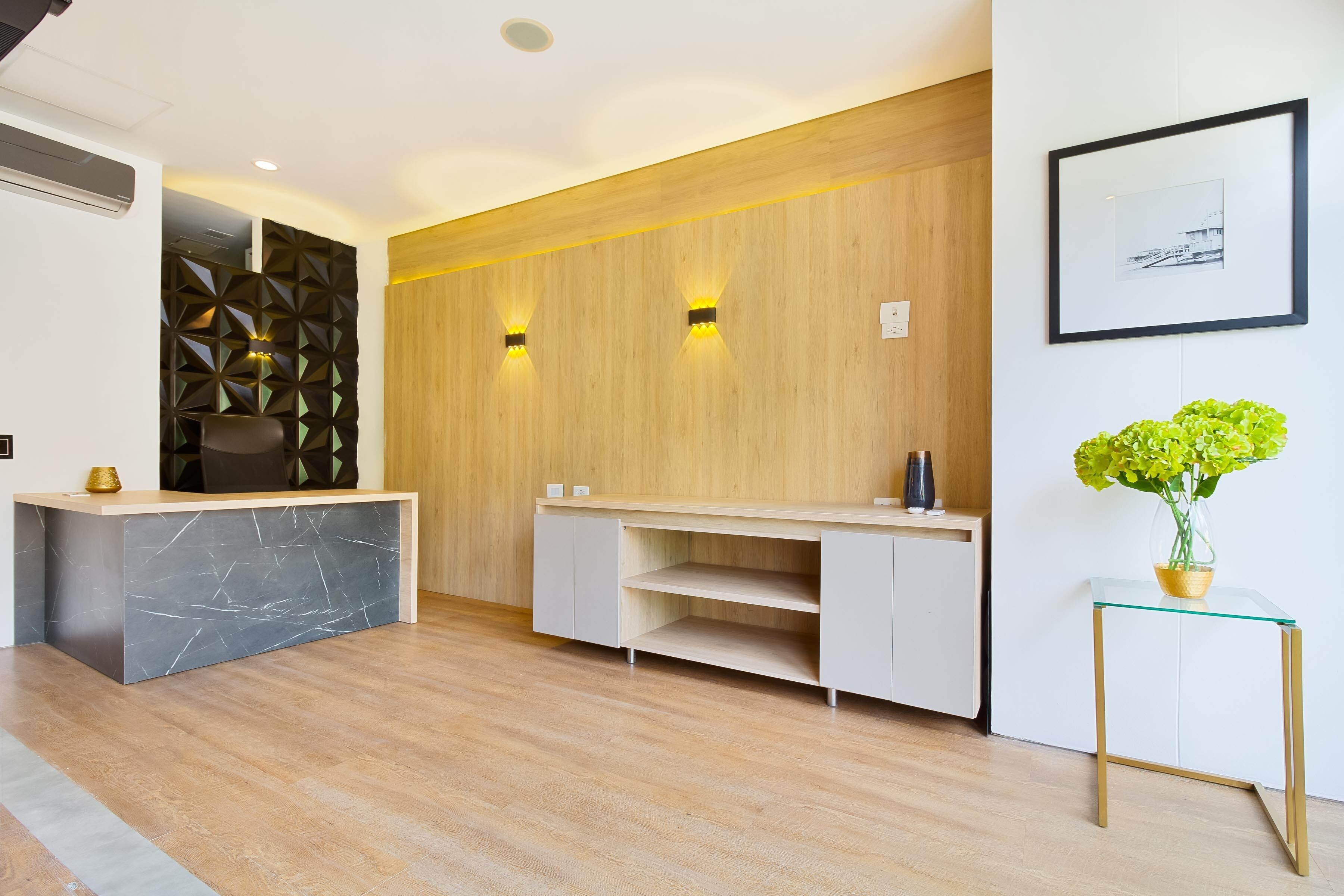 A modern reception area with a marble counter, wooden panel wall, and a glass table with a plant.