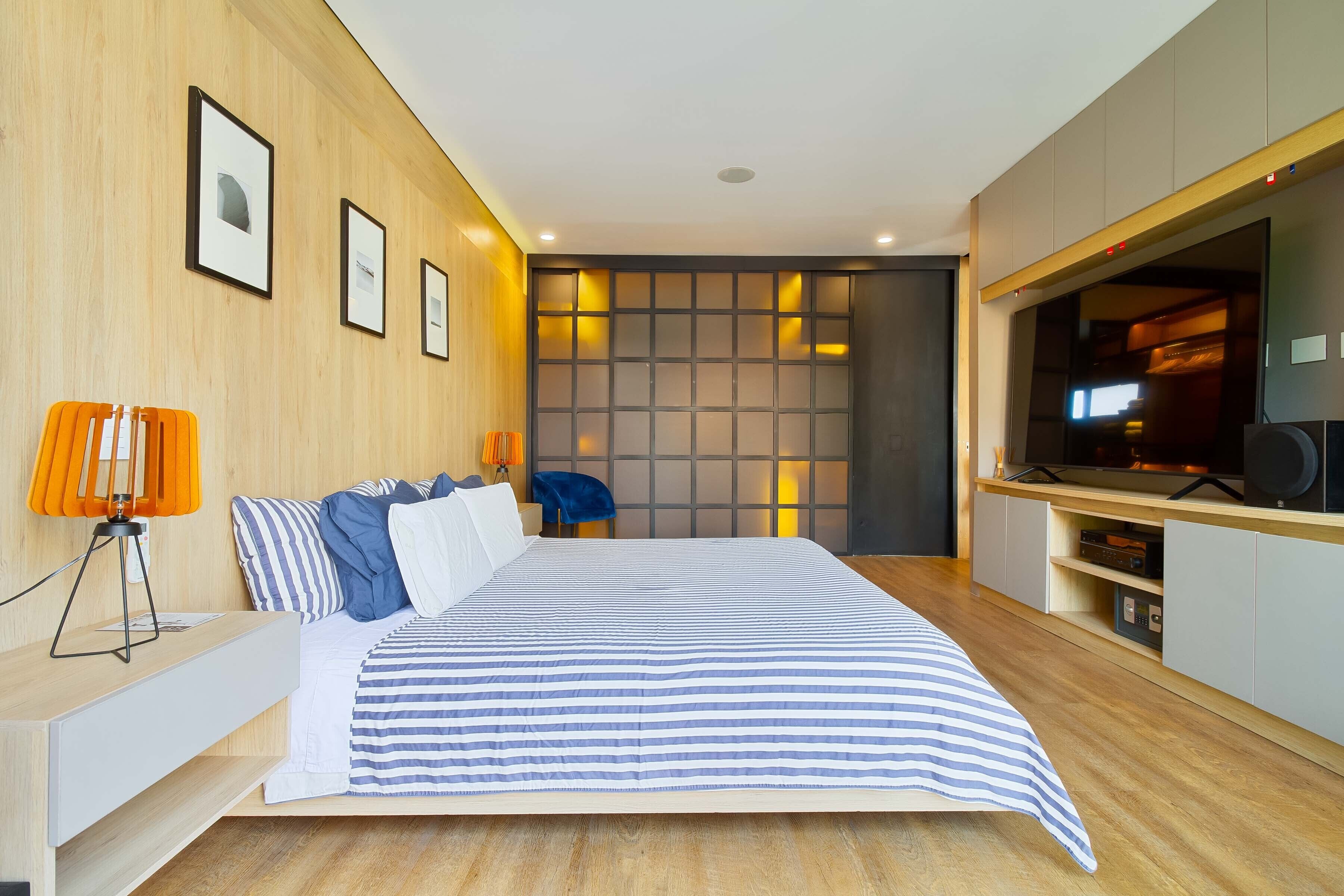 Un dormitorio moderno con una cama grande, un escritorio con lámpara, un televisor y un estante de pared.