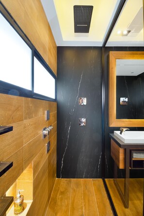 A modern bathroom with wooden and black marble walls, a large mirror, and a white sink.