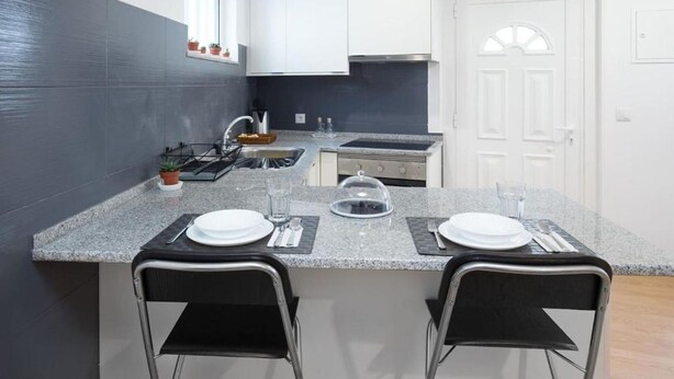 A modern kitchen with granite countertops, two black bar stools, a gas stove, and a white door in the background.