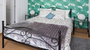 A bed with a patterned bedspread and pillows, a metal headboard, and a green floral wallpaper background.