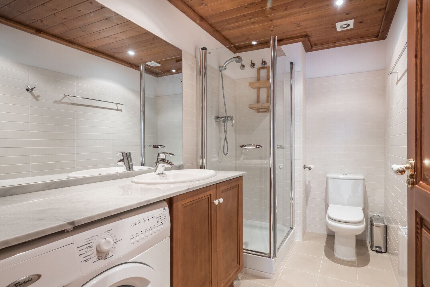 Ein modernes Badezimmer mit barrierefreier Dusche, Toilette und Waschmaschine.