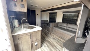 A compact RV interior with a kitchenette, a seating area, and a small entertainment unit. -  Comfortable & Private Stay in Moreno Valley (Moreno Valley)