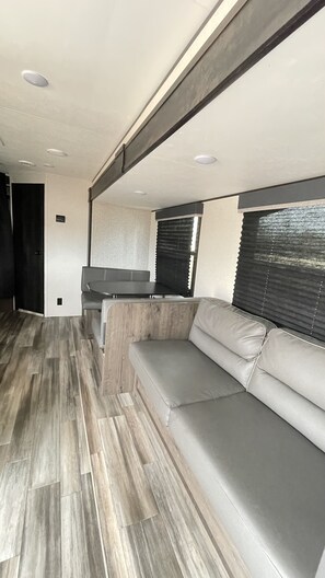 Un interior moderno de autocaravana con un sofá seccional, una mesa de comedor y una zona de cocina.