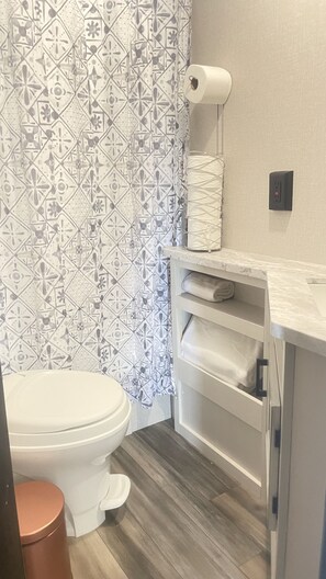 Un baño con cortina de ducha estampada, un inodoro, un perchero para toallas y una encimera de mármol.