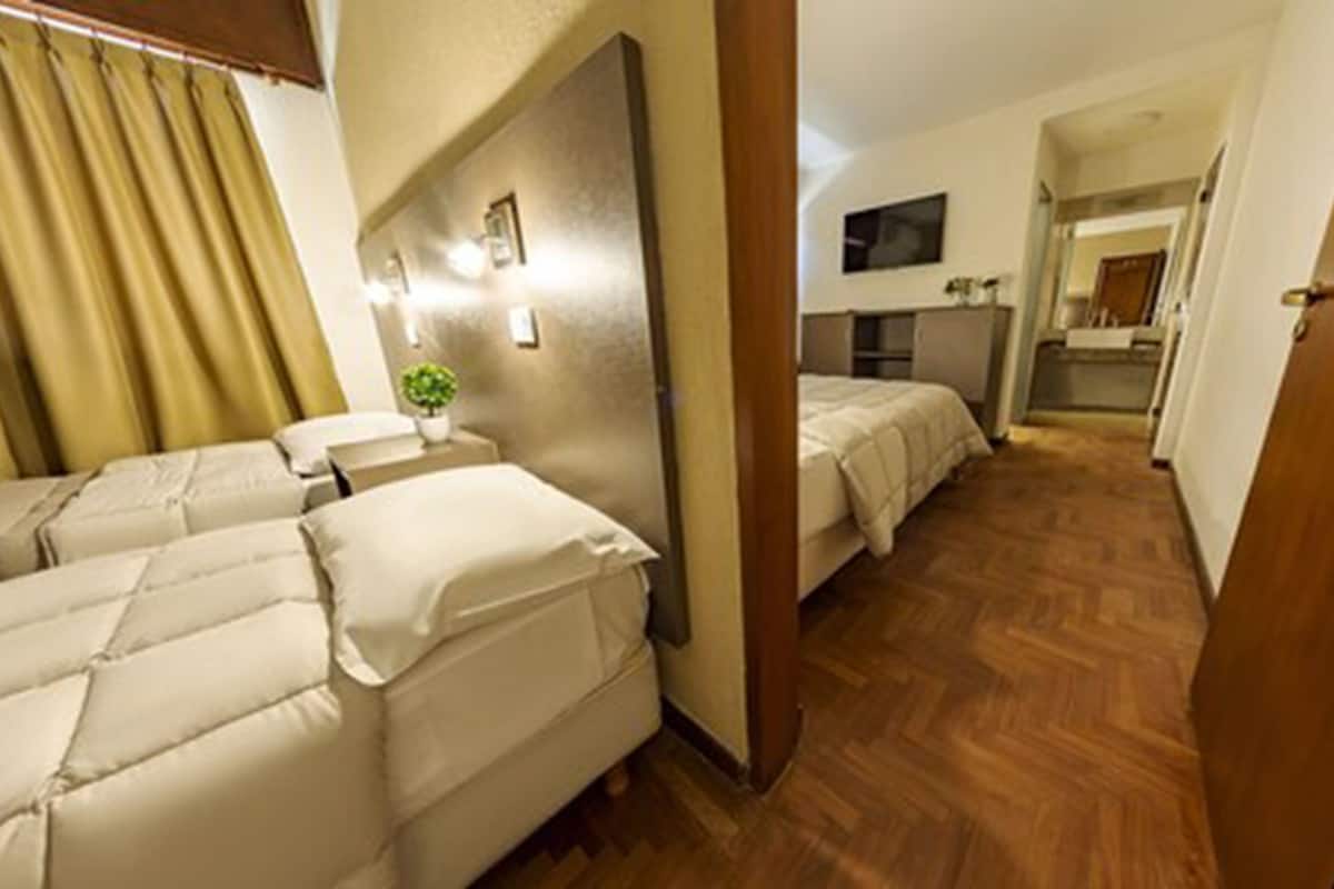 Ein Hotelzimmer mit zwei Betten, einem kleinen Tisch mit einer Pflanze, einem Spiegel und einer Küchenzeile.