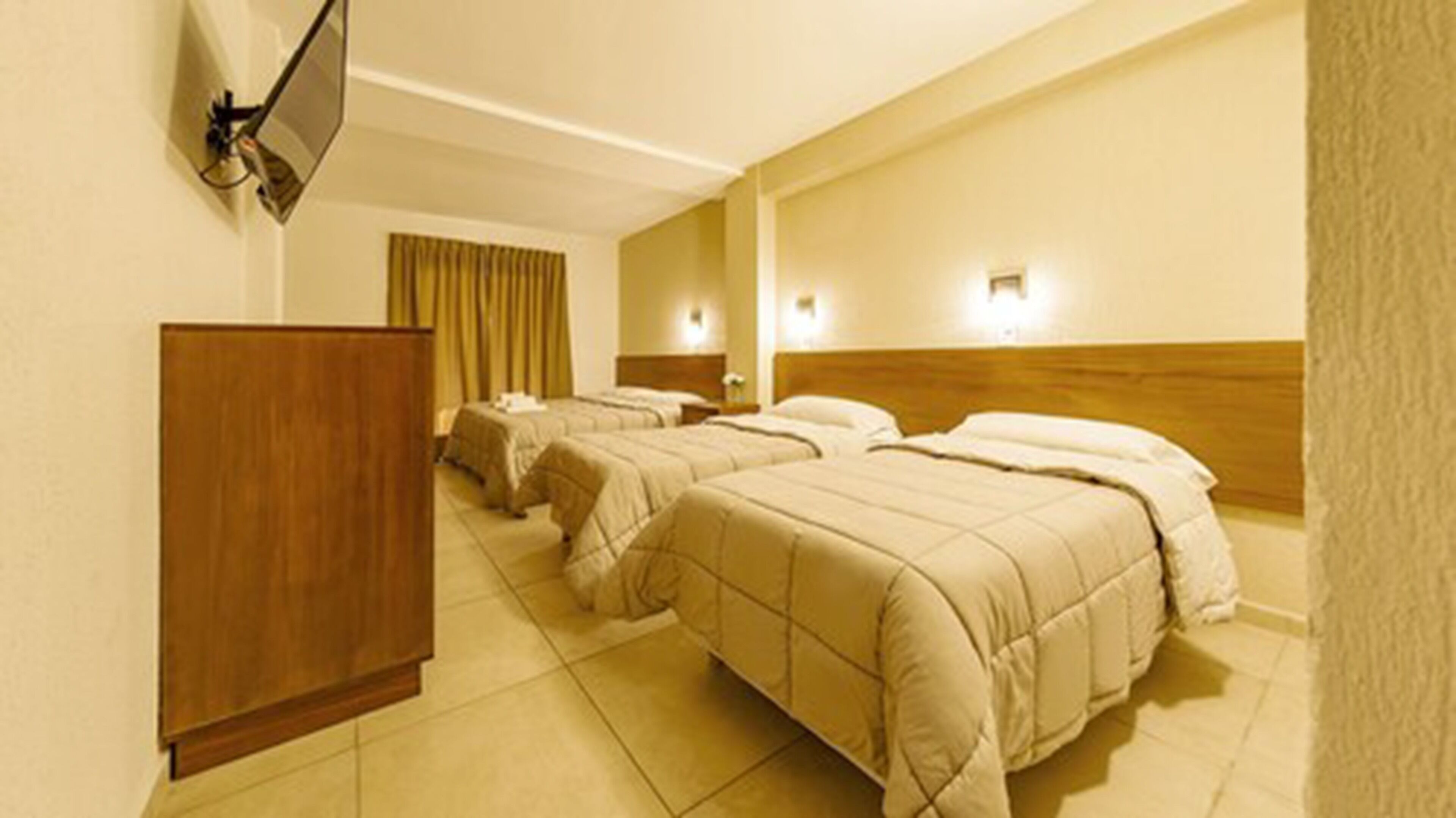A hotel room with three beds, a wooden wardrobe, and a flat-screen TV mounted on the wall.
