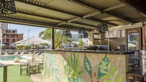 Eine Poolbar mit farbenfroher Mosaikrückwand, Sitzgelegenheiten im Freien und Blick auf Pool sowie Gebäude im Hintergrund.