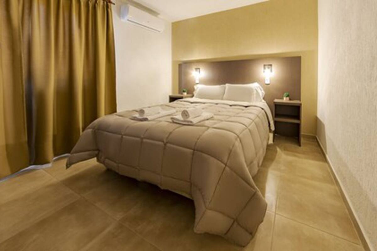 Ein Hotelzimmer mit einem großen Bett, einem Nachttisch, einer Wandleuchte und einem Vorhang.