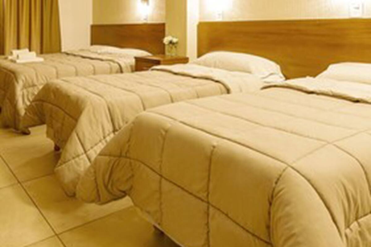 Ein Hotelzimmer mit drei Betten, jedes mit einem Holz-Kopfteil und beige farbenem Bettzeug.