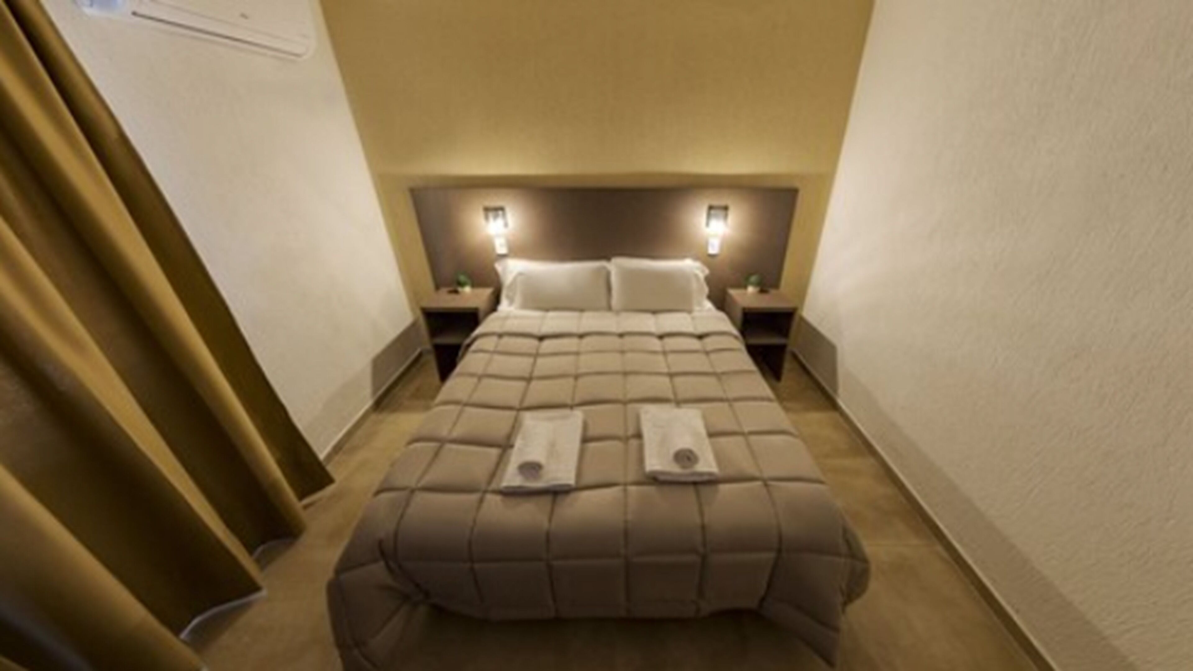 Een hotelkamer met een groot bed, twee nachtkastjes en een hoofdeinde met verlichting.