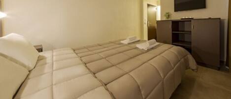 Habitación de hotel con una cama grande, un televisor de pantalla plana en la pared y un mueble minibar.
