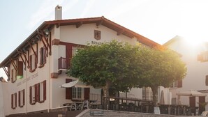 A building with a staircase leading to a door, a tree in front, and outdoor seating. - Auberge Koskenia (Bidart)