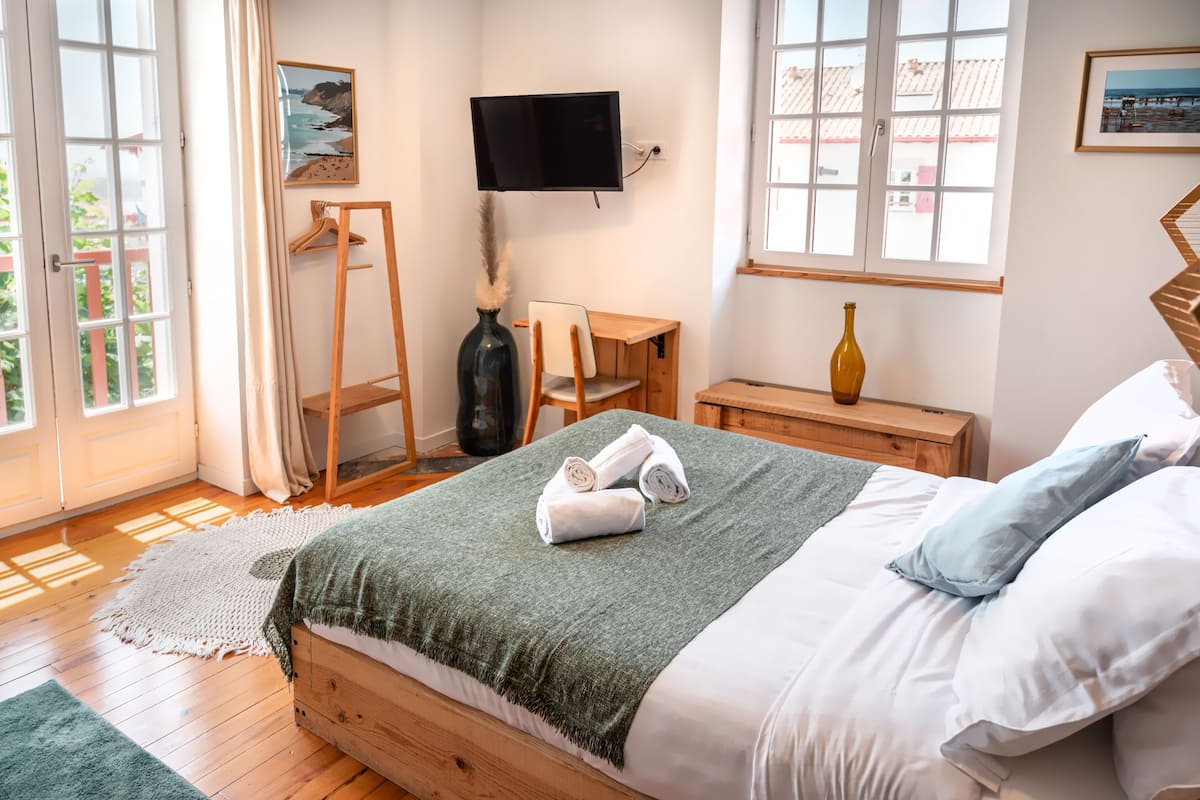 A bedroom with a bed, a TV, a desk, and a window.