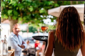 Une personne tenant un plateau sur lequel se trouve un verre, dans un espace de restauration en plein air avec des tables et des chaises.