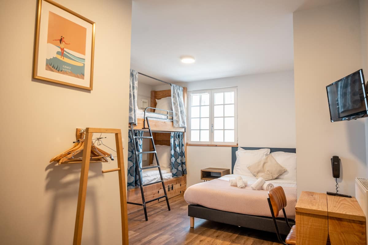 A bedroom with a bunk bed, a desk, a chair, a TV, and a window.