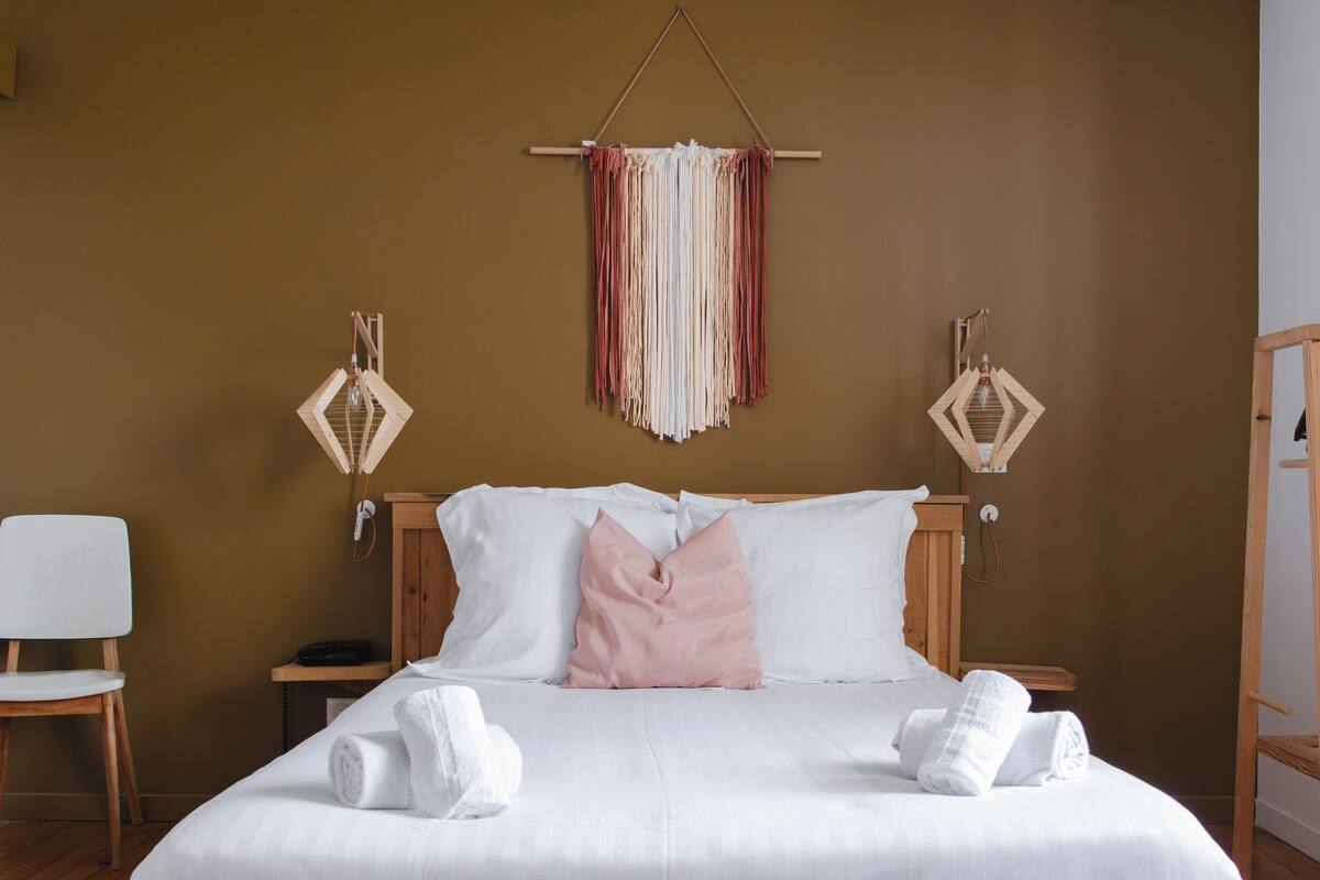 A neatly made bed with white linens and pink pillows, a wooden headboard, and a wooden nightstand with a lamp.