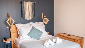 A neatly made bed with white and green pillows, a wooden nightstand with a phone, and a small wooden table with towels. - Auberge Koskenia (Bidart)