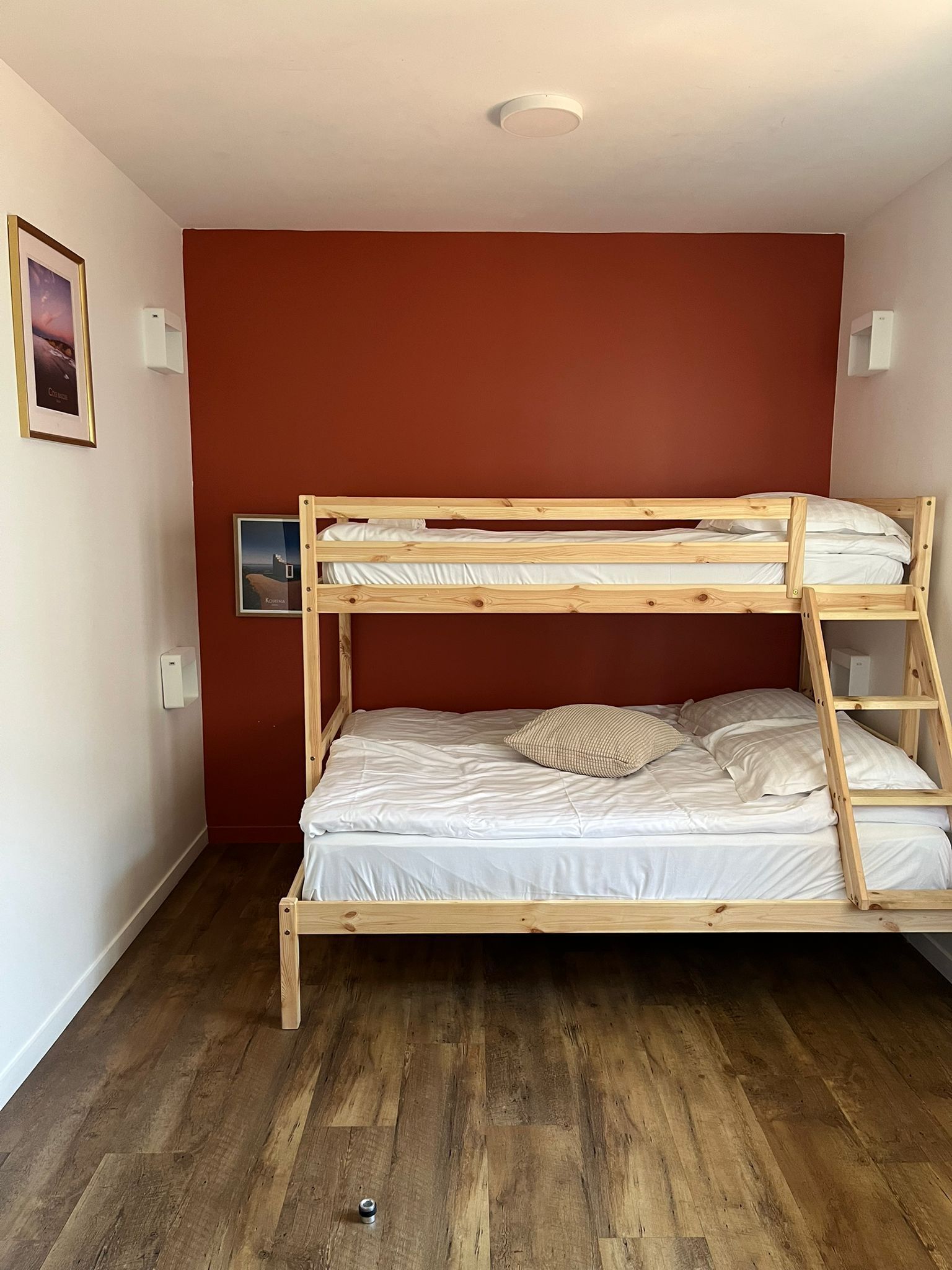 Un lit superposé avec une structure en bois, une literie blanche et un mur d’accent rouge.