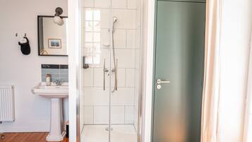 A bathroom with a glass-enclosed shower, a pedestal sink, a mirror, and a door.