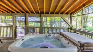 Un jacuzzi debajo de una terraza de madera, con vista a un pabellón y árboles.