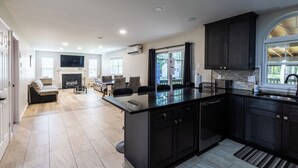 Una cocina moderna con armarios oscuros, encimera de mármol y una isla grande. Hay una zona de comedor con una mesa y sillas, y una chimenea al fondo.
