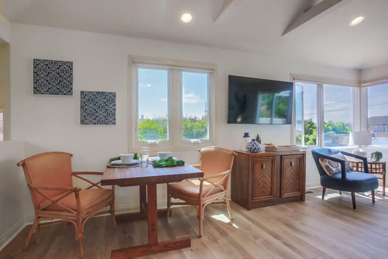 A dining area with a wooden table, two chairs, a cabinet, and a TV mounted on the wall.