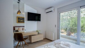 Een moderne slaapkamer met een bed, bureau, stoel, televisie en een groot raam met uitzicht op groen.