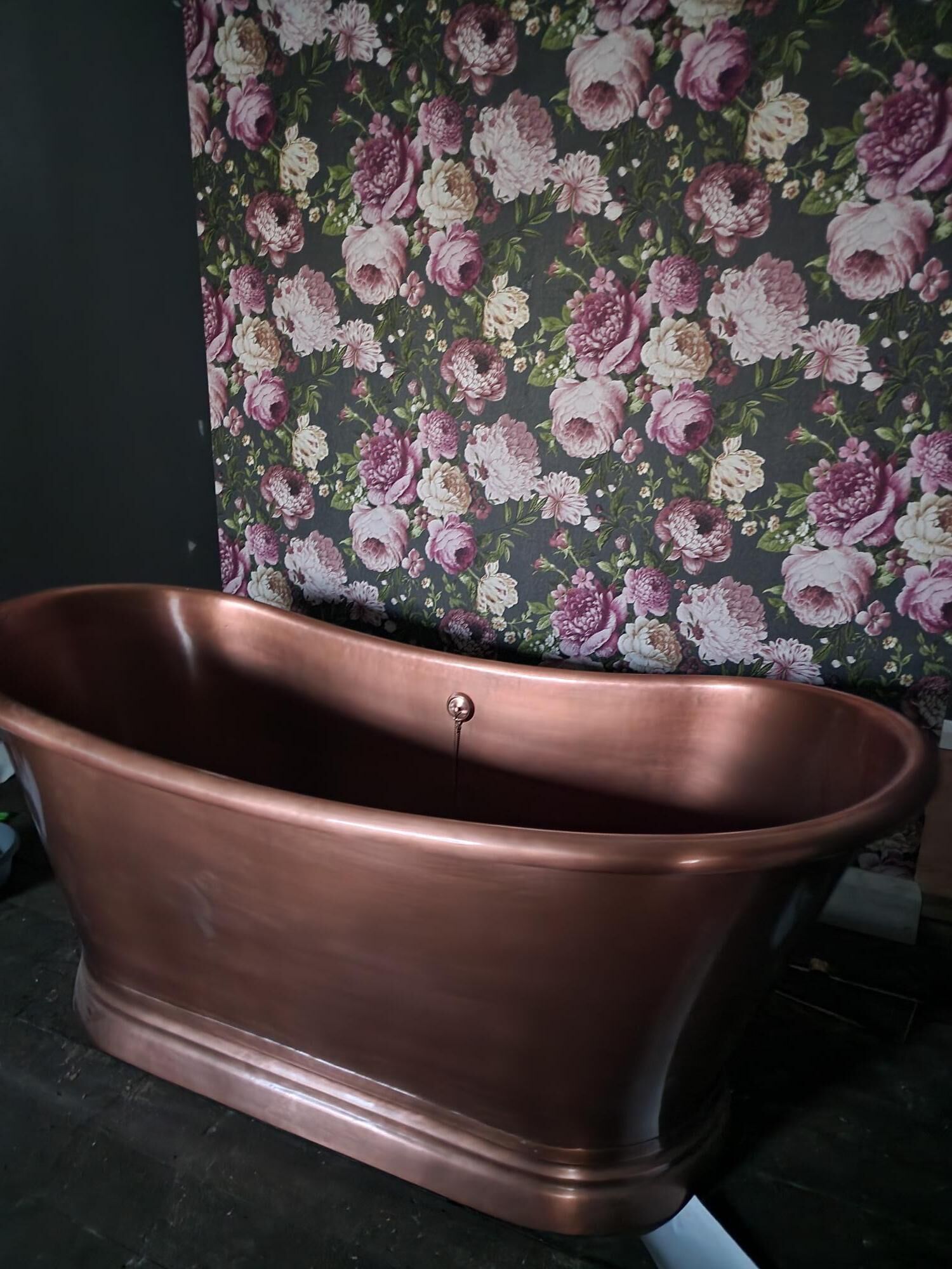Una vasca da bagno in rame in un bagno con carta da parati floreale.