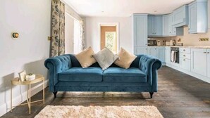 A room with a blue sofa, a small side table, and a kitchen area with light blue cabinets. - Squirrel Cottage (Ballymena)