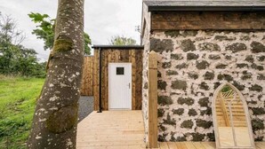 A rustic building with a stone wall, a wooden door, and a wooden archway. - Squirrel Cottage (Ballymena)