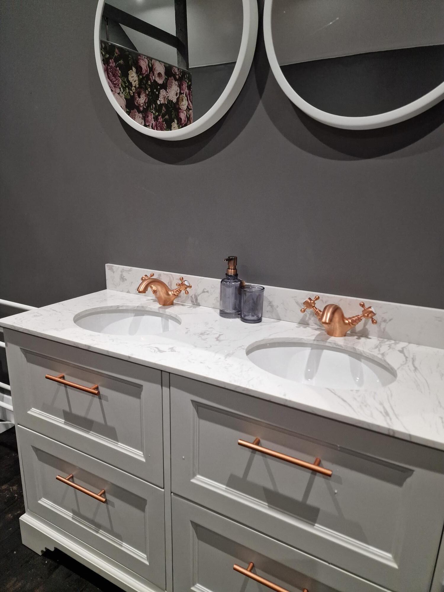 Uma toucador de casa de banho com duas pias, um espelho e um espelho decorado com padrão floral acima.